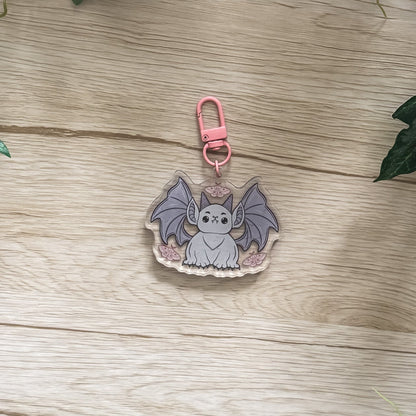 Keychain with a bat design on a wooden surface surrounded by green leaves